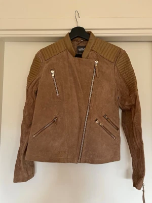 Brun biker skinnjacka från Livelo - Brun skinnjacka i bikerstil från Livelo. Äkta läder/mockamatetial, storlek 46 men skulle säga att det är snarare en S/M. (Passar mig bra som är 160 cm och har oftast S) 