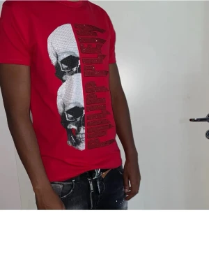 Röd Philipp Plein t-shirt med döskalle - Cool röd t-shirt från Philipp Plein med stort döskalletryck och logga framtill. T-shirten har korta ärmar och en normal passform. Perfekt för dig som vill sticka ut med en edgy stil.