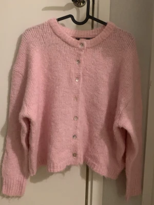 Ljusrosa kofta med knappar - Supermjuk ljusrosa kofta med långa ärmar och rund hals. Kofta har knäppning framtill med små vita skimriga knappar och ribbat tyg vid ärmslut och tröjans kant. Ger en söt look och är perfekt att ha för sig eller som en tröja över ett fint linne eller klänning. Helt oanvänd, använder inte tröjan så vill sälja den🩷