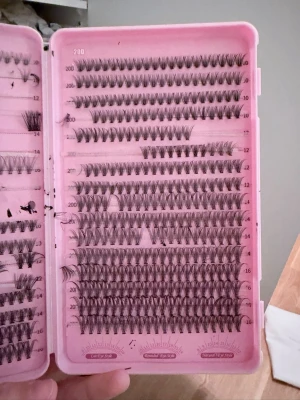 Mixade lösögonfransar i ask - Dock använda som man ser, men inte alla! Säljer en rosa ask med mixade lösögonfransar från Elashome. Fransarna är svarta, finns i olika längder och volymer, och är organiserade i rader. Perfekt för att skapa en personlig franslook. Materialet är syntetiskt och fransarna är i knippen.