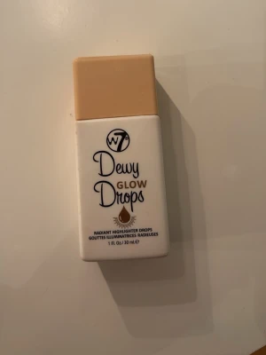 W7 Dewy Glow Drops Highlighter - Helt oanvänd! Flytande highlighter från W7 i en smidig rektangulär flaska med beige lock. Man kan blanda med en kräm innan smink för att få glow eller blanda med sin foundation! Såklart kan man använda som en vanlig highliter också!Dewy Glow Drops ger en fräsch, strålande finish och är enkel att applicera för en naturlig glow. Innehåller 30 ml och är vegansk samt cruelty free.