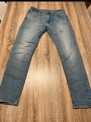 Blå raka jeans med slitningar - Snygga blå jeans med raka ben och lätt slitna detaljer på låren. Klassisk femficksmodell med bälteshällor och knappgylf. Perfekta för en avslappnad och trendig look.