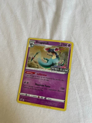Pokémonkort Dragapult Rebel Clash - Säljer ett Pokémonkort med Dragapult från Sword & Shield Rebel Clash-serien. Kortet har lila och gul ram, med Dragapult i blå och grön färg. Kortet är på engelska och har 150 HP samt specialattackerna Infiltrator och Phantom Force.