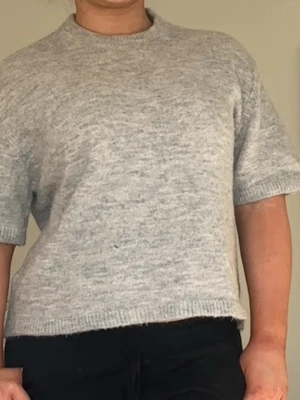 Stickad tröja  - Ljusgrå stickad t-shirttröja med korta ärmar och rund hals. Tröjan har en avslappnad passform och ribbstickade kanter vid ärmslut, hals och nederkant. Perfekt för lager-på-lager och enkel att styla till olika outfits.