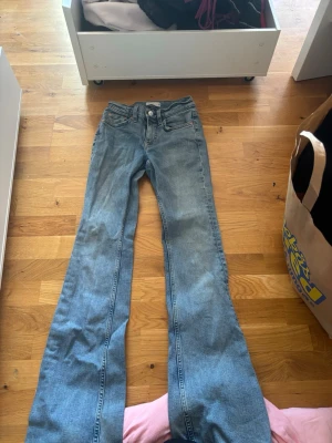 Blå utsvängda jeans från Perfect Jeans - Snygga blå jeans från Perfect Jeans med utsvängda ben och klassisk femficksmodell. Jeansen har en ljus tvätt och är tillverkade i denim. Perfekta för dig som gillar retrostil och vill ha ett par bekväma och trendiga jeans.