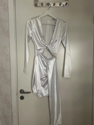 Vit omlottklänning med lång ärm - Säljer en vit omlottklänning från NA-KD i glansigt material. Klänningen har lång ärm, djup v-ringning och asymmetrisk drapering framtill. Snygg detalj med twistad midja och kortare längd. Perfekt för dig som vill sticka ut.