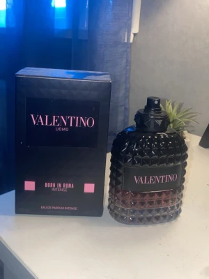 Valentino Uomo Born In Roma Intense - Valentino Uomo Born In Roma Intense är en lyxig parfym med en mörk, elegant flaska i svart och djupt röd glas med nitar och struktur. Märket Valentino står tydligt på både flaska och kartong. Perfekt för dig som vill ha en kraftfull och modern doft. Har dock använd ungefär 40 ml av den
