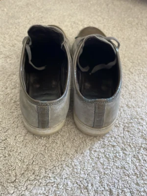 Gråa sneakers med mockadetaljer - Snygga grå sneakers med ovandel i mocka och tåparti i blankt material. Skorna har klassisk snörning och vit sula. Perfekta för en stilren och avslappnad look.
