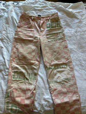 Rutiga jeans med tryck  - Unika jeans med rödvitt rutmönster och gröna tryck som 'DENIM' och 'ROUGH ENOUGH'. Vida ben. Materialet är bomull och passformen är avslappnad. Perfekta för dig som vill sticka ut med en cool streetwear-look.