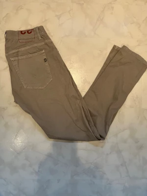 Dondup jeans - Snygga beige chinos från Dondup med klassisk femficksmodell och raka ben. Byxorna har diskreta sömmar och en liten logodetalj på bakfickan. Perfekta för dig som gillar en clean och stilren look. Materialet känns mjukt och följsamt.