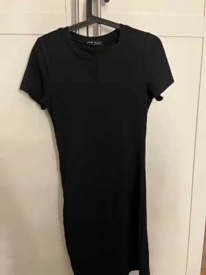 Svart ribbad kortklänning från SHEIN - En svart, ribbad kortklänning från SHEIN med rund halsringning och korta ärmar. Klänningen har en enkel och stilren design som passar perfekt till många olika looks. Tillverkad i ett mjukt och stretchigt material för skön passform.