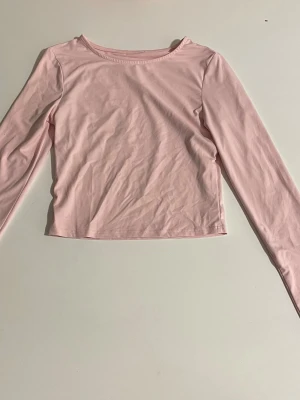 Ljusrosa långärmad topp - En enkel och stilren ljusrosa långärmad topp med rund halsringning. Toppen är croppad och har en mjuk, stretchig känsla som gör den bekväm att bära. Perfekt att matcha med jeans eller kjol för en clean look.