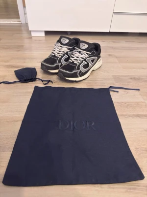 Dior B30 svarta sneakers - Dior B30 sneakers in black, size EU 44. A highly sought-after luxury sneaker with sporty design and premium comfort. The shoes are used but remain in good condition and still look great on foot. Perfect for everyday wear or to elevate a streetwear fit. Comes with original Dior dust bag and extra shoelaces, as shown in photos. Details: • Model: Dior B30 • Size: EU 43 • Color: Black / Silver details • Condition: Used (see photos for condition) • Made in Italy • Includes Dior dust bag • Extra shoel