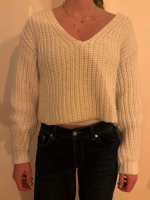 Vit stickad croppad tröja - Mysig vit stickad tröja med v-ringning och croppad passform. Tröjan har långa ärmar och ett grovt ribbstickat mönster som ger en avslappnad och trendig look. Perfekt att matcha med höga jeans.