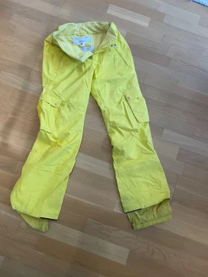 O'Neill skidbyxa - O'Neill  gula täckbyxor med cargofickor på båda benen och justerbara benslut med snölås.Perfekta för vinterns alla äventyr. Byxorna har en avslappnad passform och praktiska detaljer. 8000 mm vattenpelare