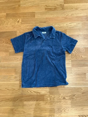 Blå frottétopp med krage Kappahl - Mjuk blå t-shirt från Kappahl i frotté med klassisk krage och korta ärmar. Perfekt för en avslappnad och chill stil. Enkel design utan mönster eller tryck, skön att bära under varma dagar. Den har inga som helst fel, bara för liten för mig. Skriv om du har någon fundering om något!