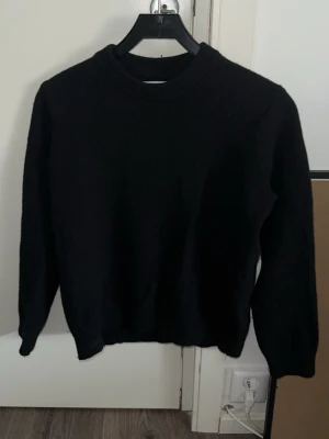 Svart stickad tröja från Samsøe Samsøe - Klassisk svart stickad tröja från Samsøe Samsøe med rund halsringning och långa ärmar. Tröjan har en enkel och stilren design som passar till det mesta. Perfekt basplagg för garderoben och lätt att matcha med olika outfits.