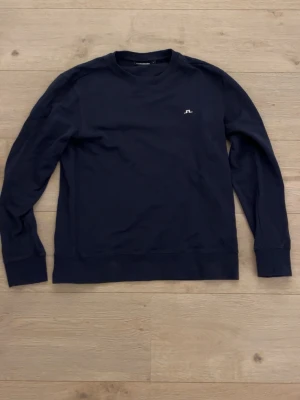 Mörkblå sweatshirt från J.Lindeberg - En stilren mörkblå sweatshirt från J.Lindeberg. I nytt skick med bra kvalitet som passar nästan vem som helst. 