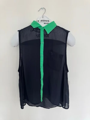 Abercrombie & Fitch - Svart transparent blus med grön krage - Snygg svart transparent blus med grön krage och knappslå. Blusen är ärmlös och har en bröstficka på vänster sida. 