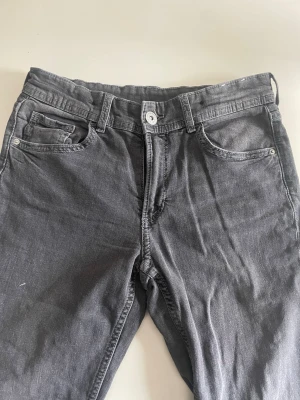 Grå flared jeans från H&M - Snygga grå jeans från H&M med flared ben och låg midja. Jeansen har justerbar midja och klassisk femficksdesign. Perfekta för dig som gillar en avslappnad men trendig look. Materialet är mjukt och stretchigt för extra komfort.