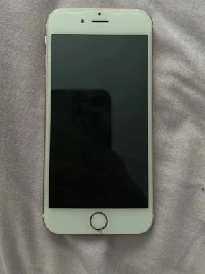 iPhone 6s i roséguld - Säljer en iPhone 6s i snygg roséguld-färg. Telefonen har en klassisk rund hemknapp med Touch ID och en 4,7-tums skärm. Baksidan är i metall med Apple-loggan och kameran sitter uppe till vänster. Perfekt för dig som gillar stilren design och smidigt format.