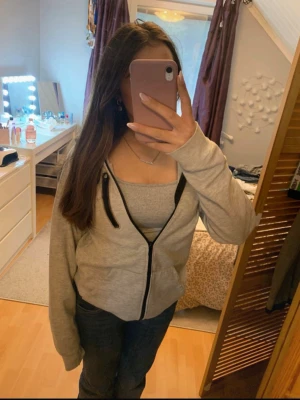 Grå hoodie med svart dragkedja - Säljer en grå hoodie med svart dragkedja och huva. Hoodien har en extra dragkedjeförsedd ficka på bröstet och är tillverkad i mjukt material. Perfekt för en avslappnad och cool look. Det står xs men jag skulle säga att den är S. 