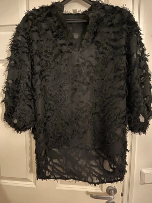 Svart transparent topp från Soaked - Säljer en svart transparent topp från Soaked med coola fransdetaljer över hela plagget. Toppen har korta ärmar och en lös passform, perfekt för dig som vill sticka ut lite extra. Materialet känns lätt och luftigt.