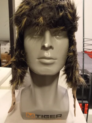 Brun pälsmössa från Handskkompaniet - Storlek S  - Säljer en riktigt snygg brun pälsmössa från Handskkompaniet. Mössan har rutigt mönster upptill, detaljer i manchester och fuskpäls runt kanterna. Utrustad med knappar och små fickor på sidorna för extra stilpoäng.