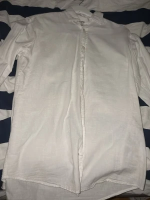 Vit linneskjorta från Essentials S - Klassisk vit skjorta från Essentials i luftigt linne. Skjortan har normal passform, lång ärm och knappar framtill. Perfekt till sommaren med sin lätta känsla och stilrena look. Mandarin-krage för en modern touch.