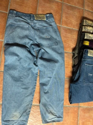 Blå raka jeans från Dime - Säljer ett par klassiska blå jeans från Dime med rak passform och hög midja. Jeansen har fem fickor, bälteshällor och en snygg patch med logga bak i midjan. Perfekta för en avslappnad och stilren look.