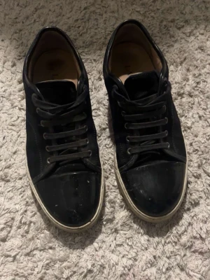 Svarta Lanvin lädersneakers - Svarta sneakers från Lanvin i läder med klassisk låg siluett och vita sulor. Skorna har svarta skosnören och diskret branding på innersulan. En stilren modell för dig som gillar exklusiva och minimalistiska sneakers.