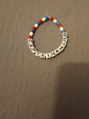 Färgglatt pärlarmband CAPTAIN#HARD - Säljer ett handgjort armband med vita bokstavspärlor som stavar CAPTAIN#HARD. Armbandet har runda pärlor i rött, blått och vitt. Perfekt accessoar för dig som vill sticka ut med ett personligt smycke.