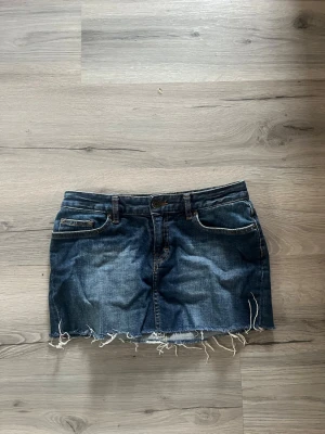 Blå jeanskjol med rå kant - Säljer en blå jeanskjol med en fransig kant ner till. Bra skick inte använd speciellt mycket. Storlek 36