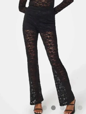 Svarta spetsbyxor  - Säljer ett par svarta byxor i spets med utsvängda ben. Materialet är stretchigt och transparent med blommigt spetsmönster. Perfekta för dig som vill sticka ut med en trendig look.