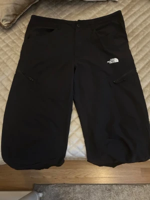 Svarta Byxor - The North Face - Säljer ett par svarta täckbyxor från The North Face med dragkedjeförsedda fickor på sidorna och logga på vänster lår. Storlek: W36 & L32