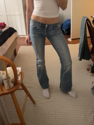 Ljusblå bootcut jeans - Säljer ett par ljusblå bootcut jeans med klassisk femficksdesign och låg midja. Jeansen har en lätt utsvängd passform nedtill och stängs med dragkedja och knapp. Perfekta för en avslappnad och trendig look. Lite korta för mig som är 170, perfekt för dig som är ca 165!