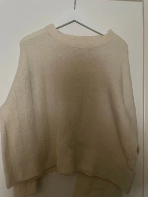 Beige stickad tröja med ribbmönster - Säljer en beige stickad tröja med diskret ribbmönster. Tröjan har rund hals och långa ärmar, perfekt för att hålla sig varm. Materialet är mjukt och bekvämt, passar dig som gillar enkel och stilren design. Den passar s/m