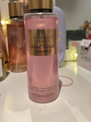 Velvet Petals Shimmer mist - En shimmer body mist från Victoria's Secret i doften Velvet Petals. Flaskan är rosa med guldigt lock och etikett. Ger en glittrande finish och har noter av blommor och mandel. Innehåller 250 ml och är perfekt för dig som vill dofta gott och glänsa lite extra. Endast testad typ 2 sprut, köptes för 300