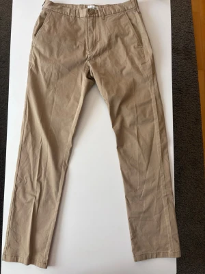 Beiga chinos med rak passform - Snygga beiga chinos med rak passform och klassisk design. Byxorna har knapp- och dragkedjestängning samt bälteshällor i midjan. Tillverkade i ett mjukt och lätt bomullsmaterial som ger en avslappnad look. Perfekta för dig som gillar stilrena och enkla plagg. Från brothers