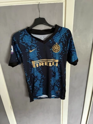 Inter Milan matchtröja Lukaku #9  - Snygg Inter Milan matchtröja med Lukaku och nummer 9 på ryggen. Tröjan är svart med blått pixelmönster, guldiga detaljer och Pirelli som sponsor på bröstet. Korta ärmar och klubbmärke på vänster sida. Perfekt för fotbollsfans!