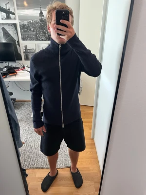 Mörkblå ribbad ziptröja - En mörkblå ribbad ziptröja med hög krage och hel dragkedja framtill. Tröjan är använd 2 gånger, således nyskick med inga defekter. 