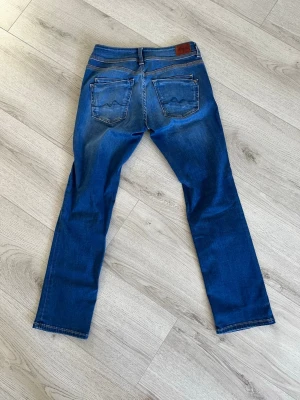 Pepe Jeans - Snygga blå jeans från Pepe Jeans med klassisk femficksdesign. Jeansen har slitningar och ljusare partier på baksidan samt läderpatch med logga i midjan. Perfekta för en avslappnad och trendig look.