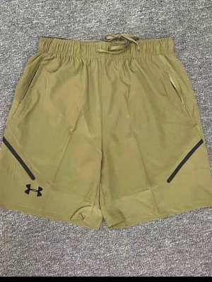 Beiga träningsshorts från Under Armour - Snygga beiga träningsshorts från Under Armour med svarta detaljer och logga. Shortsen har elastisk midja med snörning och två sidofickor. Perfekta för gymmet eller löprundan.