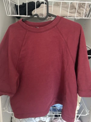Vinröd oversized hoodie utan huva - En enkel och oversized vinröd hoodie i mjukt bomullsmaterial. Tröjan har raglanärmar och rund halsringning. Inga synliga loggor eller tryck, perfekt för en chill och avslappnad stil.