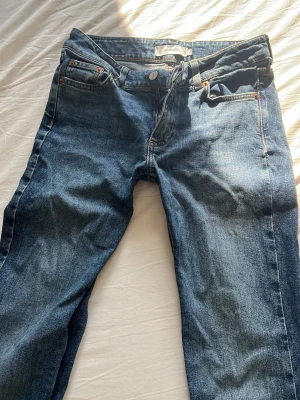 Mörkblå bootcut jeans - Säljer ett par mörkblå bootcut jeans med klassisk femficksdesign och orangea sömmar. Jeansen har normal midja och dragkedja med knapp. Materialet är kraftig denim i bomull. Perfekta för dig som gillar en tidlös look.
