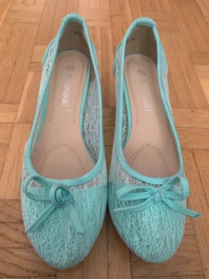 Turkosa ballerinaskor med spetsdetaljer - Snygga turkosa ballerinaskor från Diamant med spetsdetaljer och liten kilklack. Skorna har rund tå, dekorativ rosett framtill och är tillverkade i ett mesh-liknande material som ger en luftig känsla. Perfekta för dig som vill ha något unikt och fräscht till din outfit.