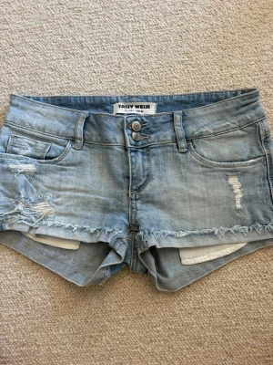 Ljusblå denimshorts från Tally Weijl - Säljer ett par ljusblå denimshorts från Tally Weijl med fransiga kanter och slitna detaljer. Shortsen har fem fickor, bälteshällor och dubbla knappar framtill. Perfekta för varma dagar och en avslappnad look.💓