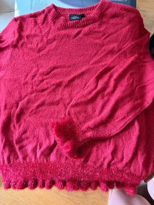 Röd stickad tröja med volangkant - Säljer en röd stickad tröja från KappAhl med volangdetaljer och glittrig kant vid ärmslut. Strl L