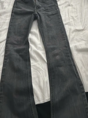 Grå bootcut jeans med slitningar - Säljer ett par grå bootcut jeans med lätt slitna detaljer och klassisk femficksmodell. Jeansen har en något utsvängd passform nedtill och är tillverkade i ett mjukt denimtyg. Perfekta för en avslappnad och trendig look.
