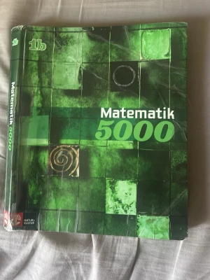 Matematik 5000 1b kursbok - Matematik 5000 1b är en kursbok för gymnasiet, perfekt för dig som pluggar matte på högre nivå. Boken har ett grönt omslag med rutmönster och abstrakta symboler. Utgiven av Natur & Kultur och används ofta i svenska skolor.